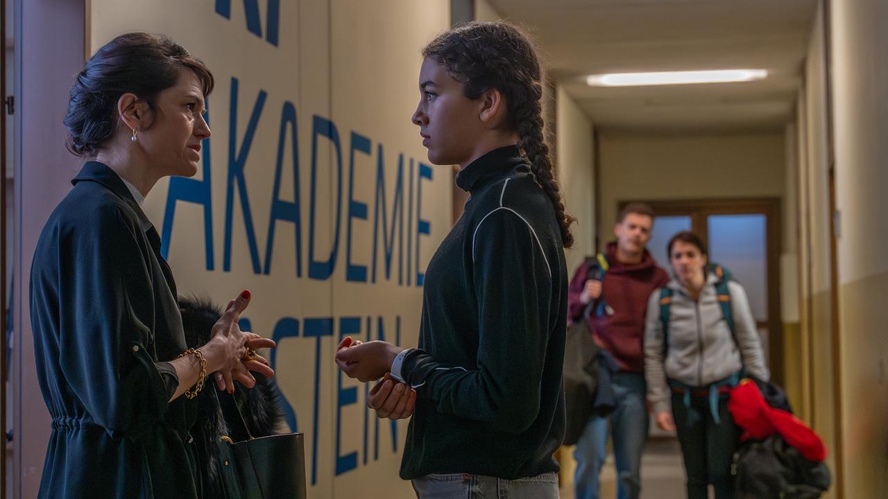 Sofia Ammann und Nawal Ammann stehen in einem Schulflur, während Albin und Tina im Hintergrund zu sehen sind.