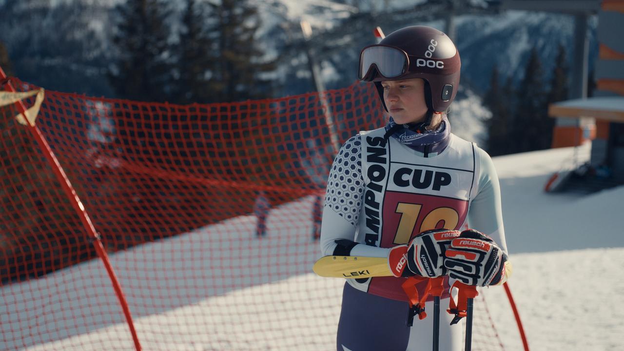 Dani Strobl im Skirennanzug und mit Helm steht mit Skistöcken vor einem roten Sicherheitsnetz auf der Piste.