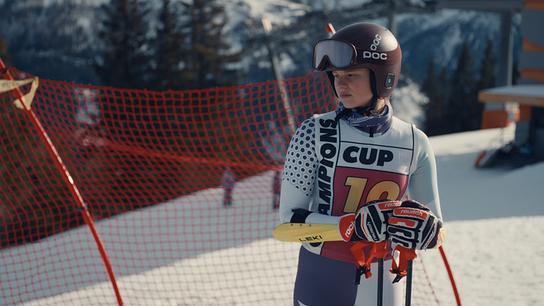 Dani Strobl im Skirennanzug und mit Helm steht mit Skistöcken vor einem roten Sicherheitsnetz auf der Piste.