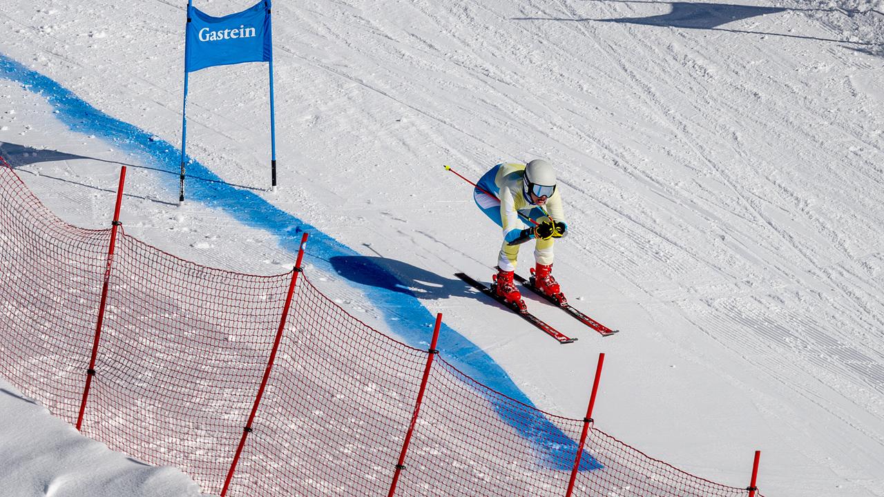 Ein Skirennläufer fährt bei Sonnenschein in Rennposition durch einen markierten Kurs.