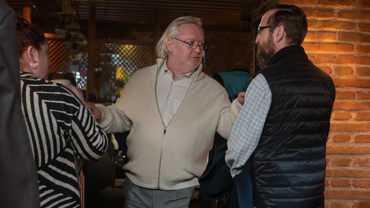 Schiesstl mengt sich zwischen Petra und dem Bürgermeister in einem Gasthaus und hält sie beiden an ihren Oberarmen.