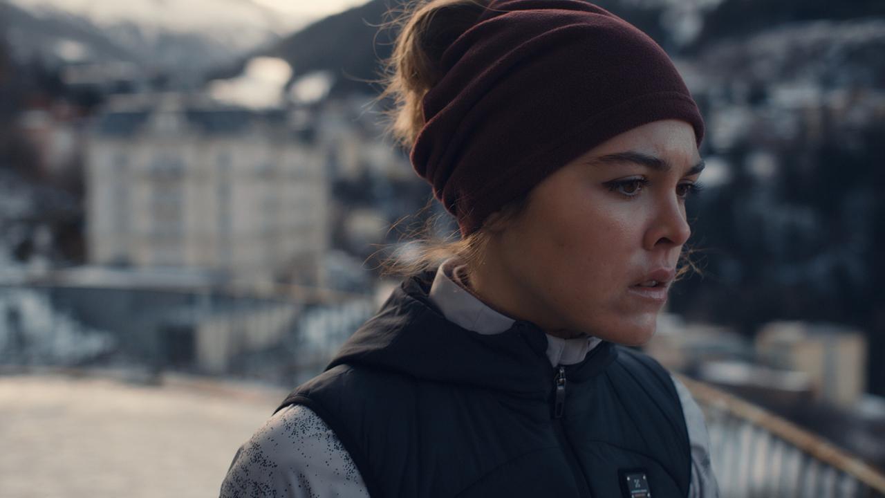 © ORF/BR/Superfilm Solenn Eden steht draußen an einem Geländer mit winterlicher Bergkulisse im Hintergrund.