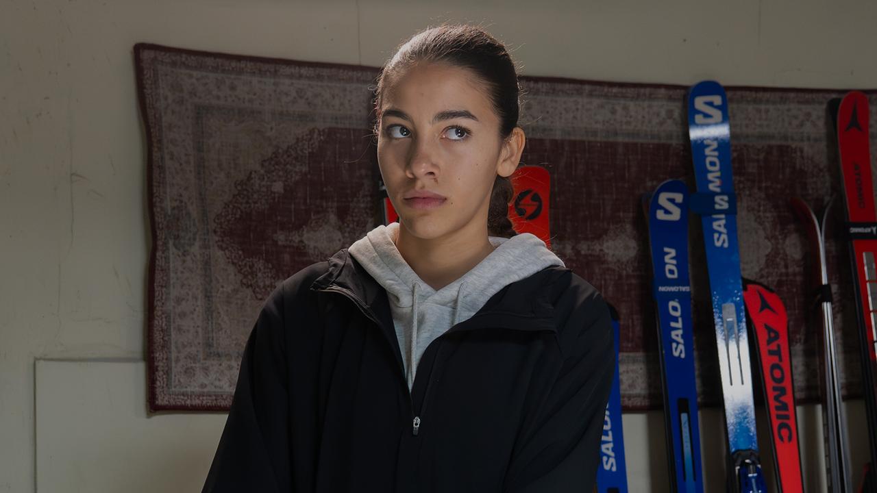 © ORF/BR/Superfilm/Stefanie Leo Nawal Ammann steht in einem Raum mit Skiern an der Wand.