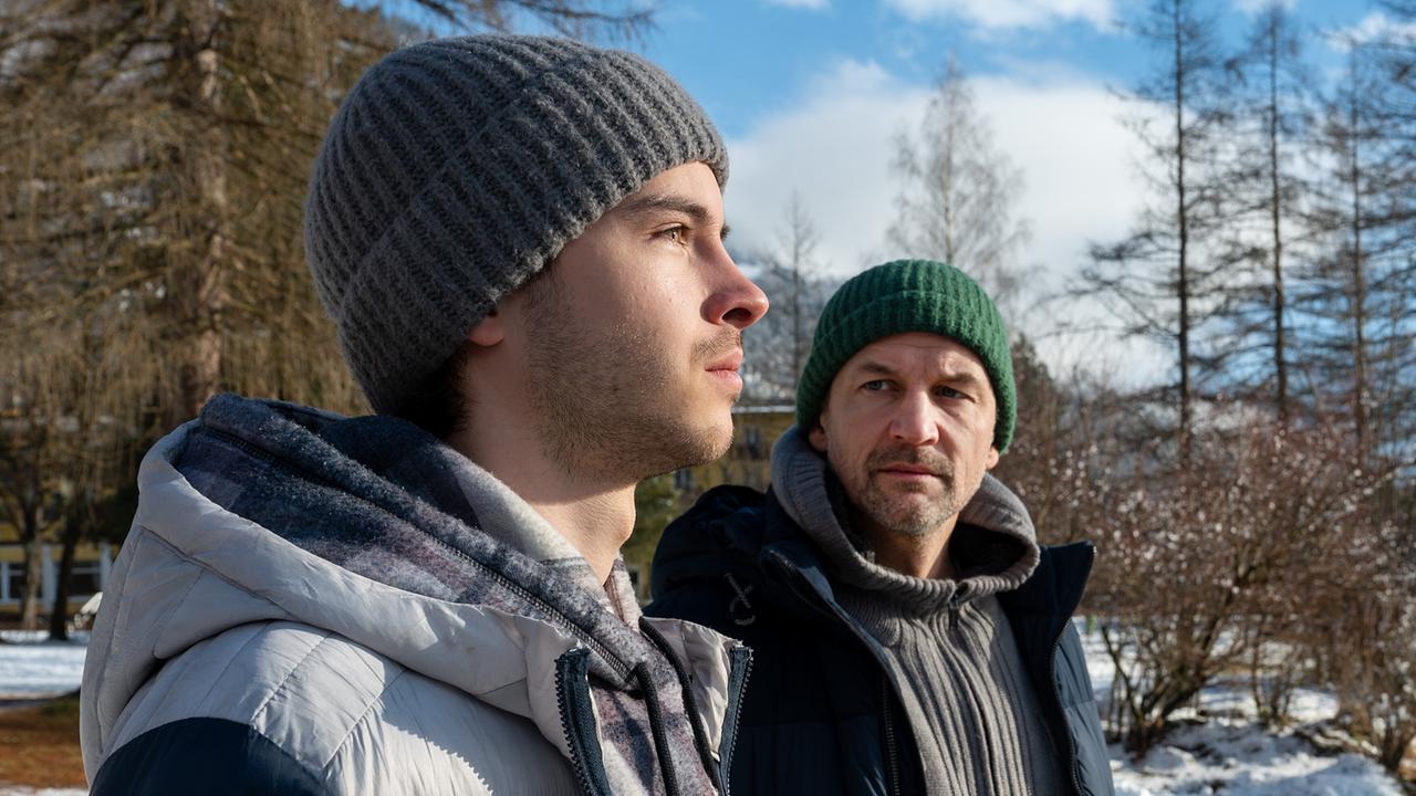 Luca Rossi und Mario Rossi stehen im Freien und blicken sich an an einem sonnigen Wintertag.