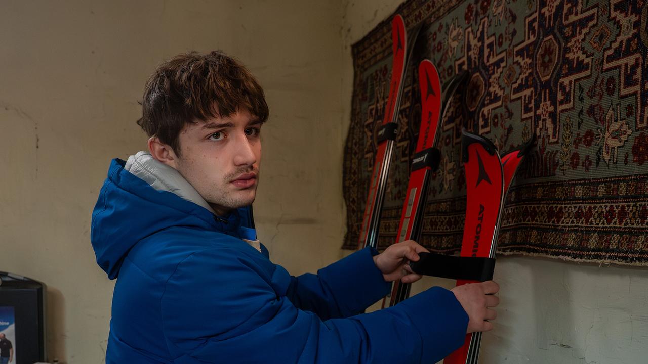 Nikki Auer nimmt ein Paar Skier, die an einer Wand an einem Wandperserteppich gelehnt sind.