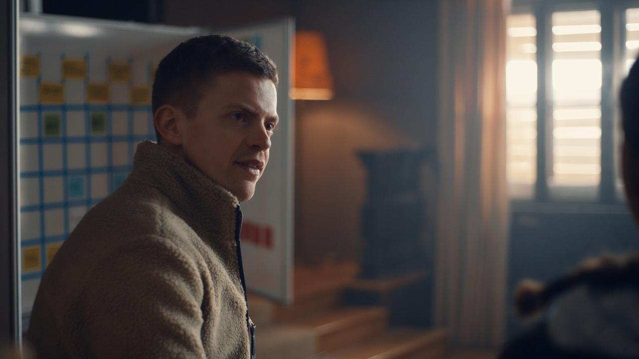 Albin steht in einem Innenraum vor einer Tafel mit farbigen Notizzetteln.