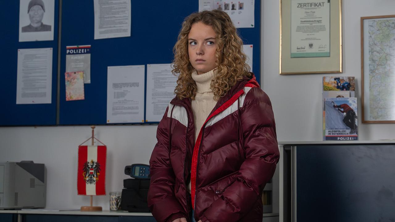 Steffi Strobl steht in einem Polizeibüro vor einer Wand mit Dokumenten und Urkunden und schaut ernst.