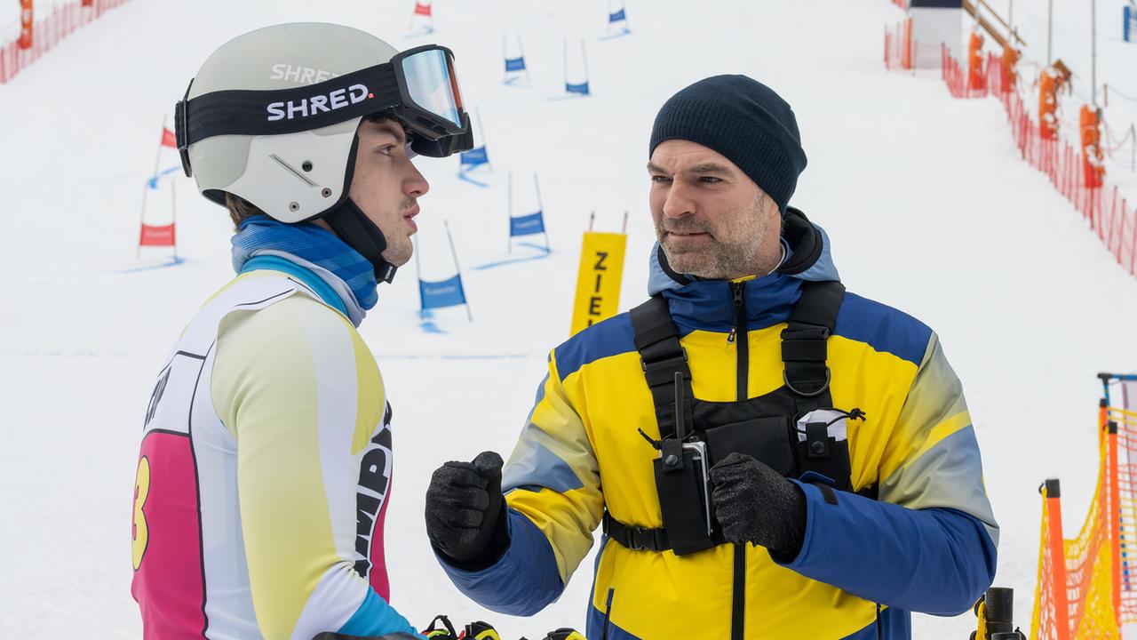 Mark Auer spricht motivierend mit Nikki Auer im Skirennanzug vor einer verschneiten Piste.