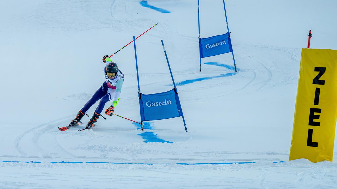Ein Skirennläifer rast dynamisch durch einen Riesenslalomkurs und legt sich kurz vor dem Ziel stark in die Kurve.
