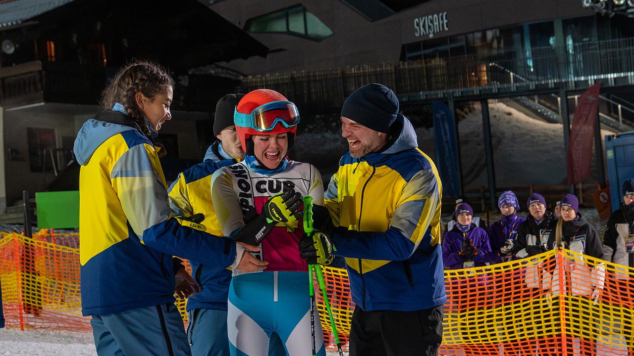 Nawal Ammann, Nikki Auer und Mark Auer bejubeln die Skirennläuferin Solenn Eden im beleuchteten Zielbereich bei Nacht.