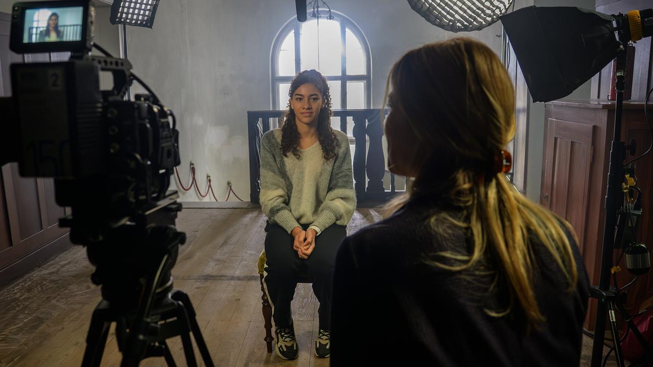 Nawal Ammann wird von Julia Traube in einem rustikalen Raum inmitten eines professionellen Filmsets mit Kamera, Scheinwerfern und Tonangel interviewt.