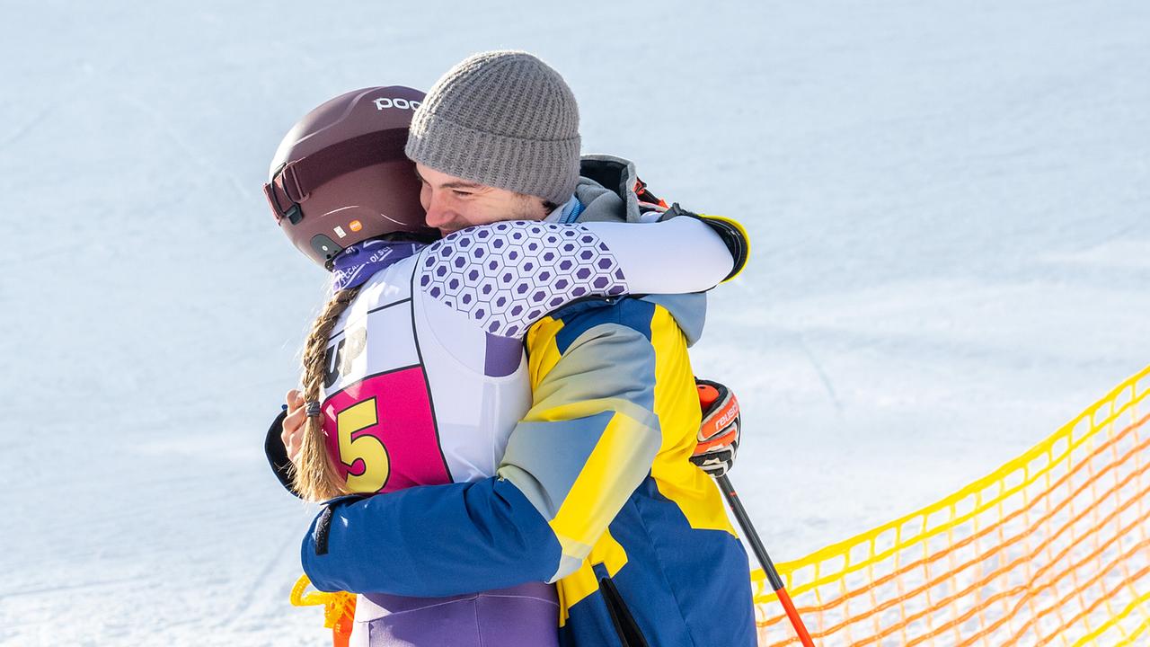 Dani Strobl und Luca Rossi umarmen sich herzlich auf der Piste vor einer Absperrungen und winterlicher Bergkulisse.