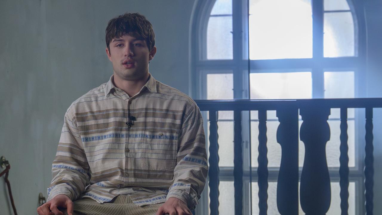 Nikki Auer sitzt in einem hellen, leicht verstaubten Raum vor einem großen Rundbogenfenster und trägt ein am Kragen befestigtes Mikrofon für ein Interview.