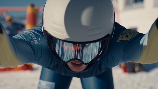 Skirennläufer Nikki Auer beugt sich im Startgate kraftvoll nach vorne, bereit zum Rennstart.