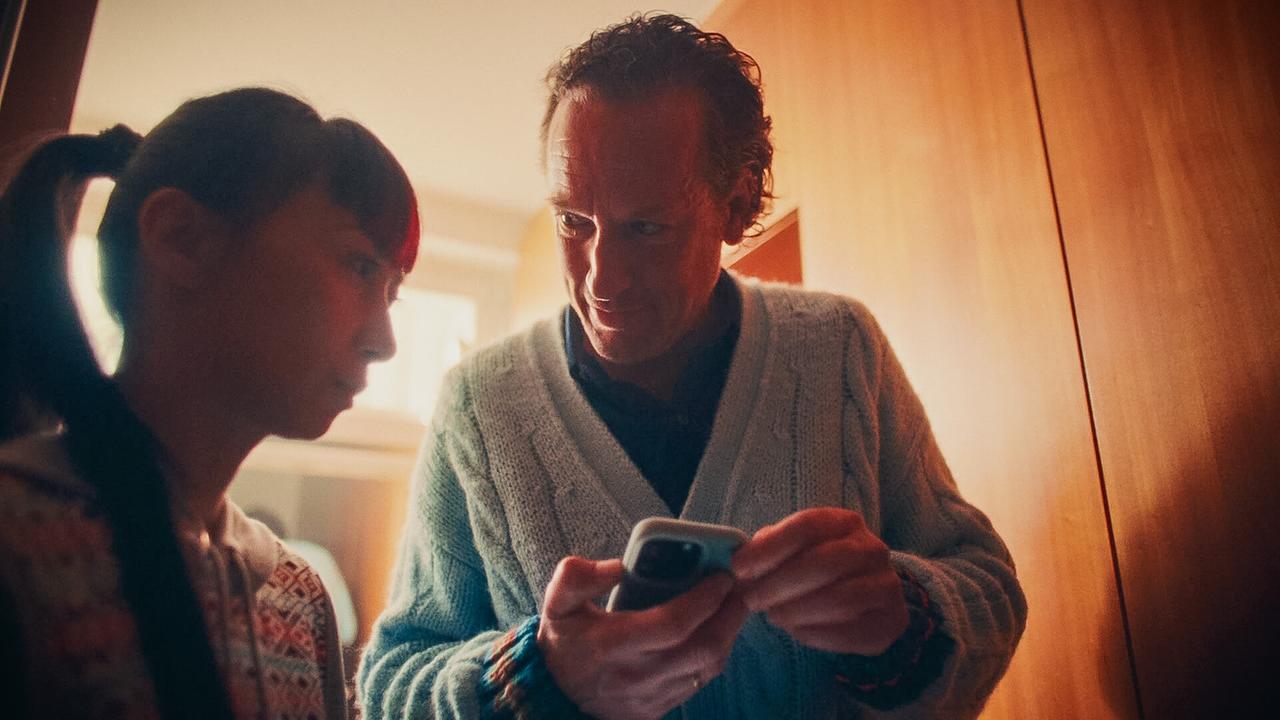 Jonathan zeigt Saya etwas auf seinem Smartphone in einem wohnlichen Raum.