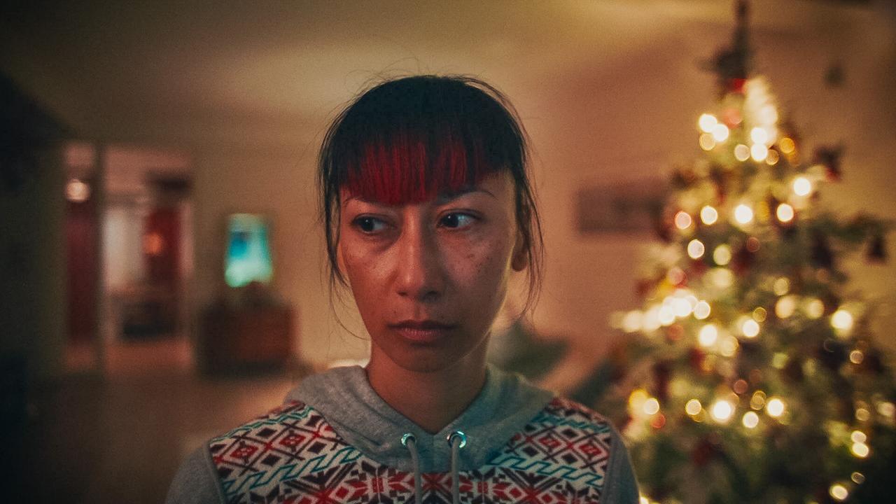 Saya steht vor einem weihnachtlich geschmückten Christbaum in einem warm beleuchteten Wohnzimmer.