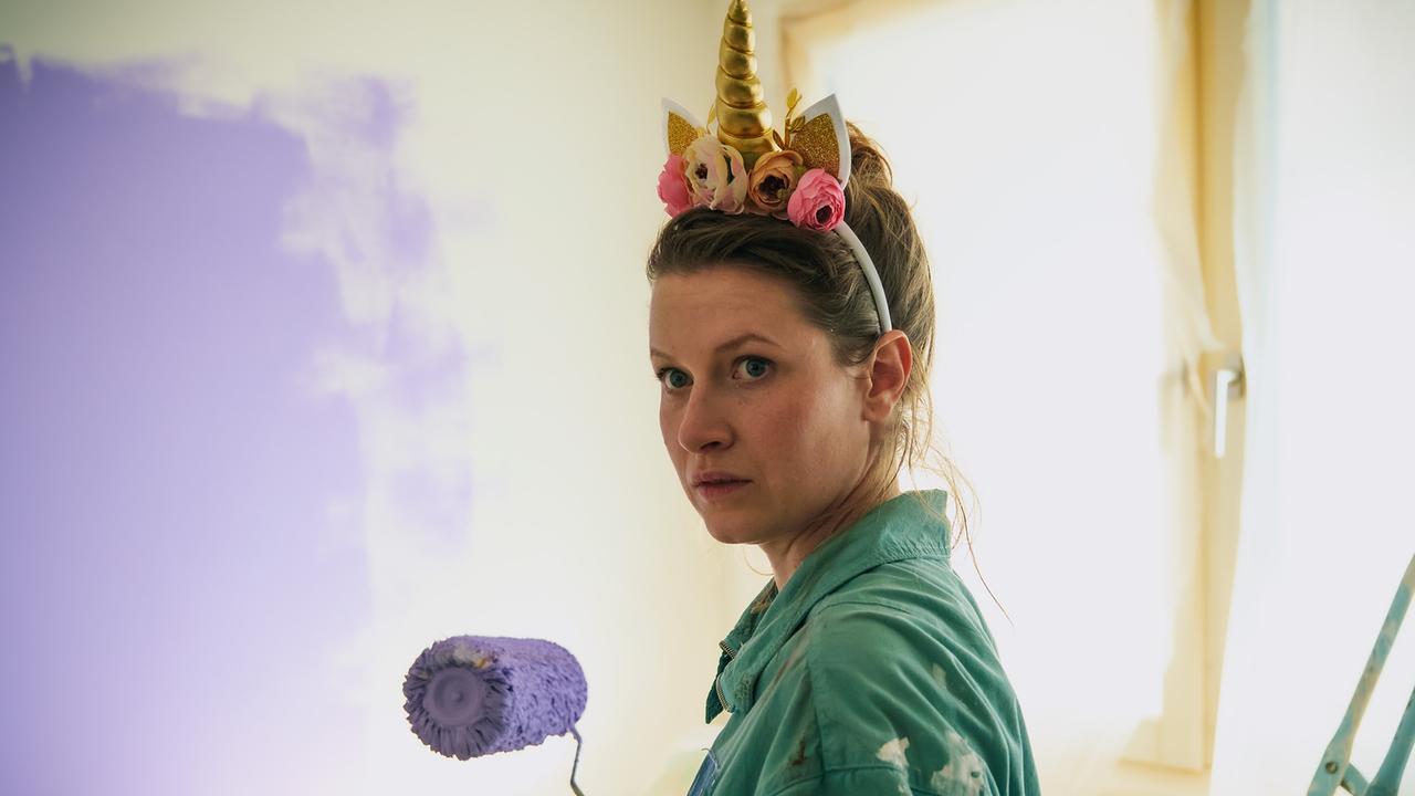 Anna mit einem Einhorn-Haarreif streicht eine Wand mit lilafarbener Farbe.