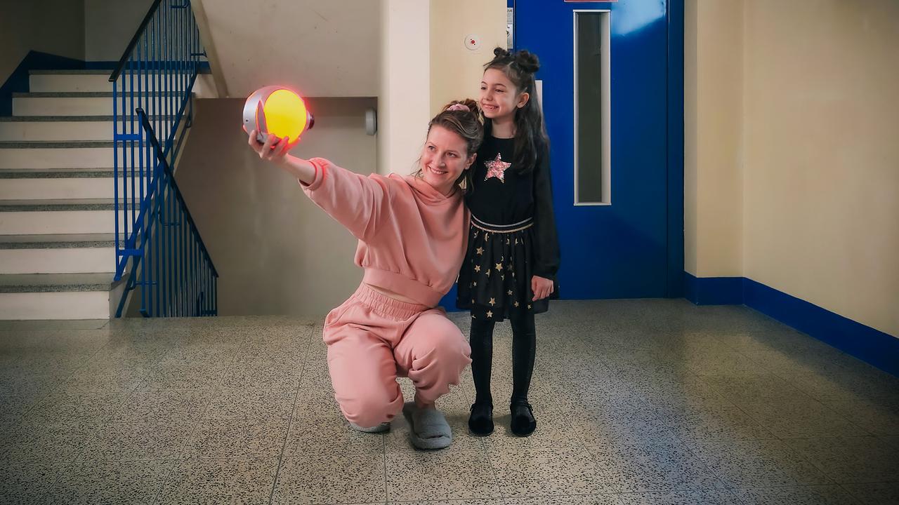 Anna in rosa Freizeitkleidung kniet neben Mia und hält ein leuchtendes rundes Gerät hoch.