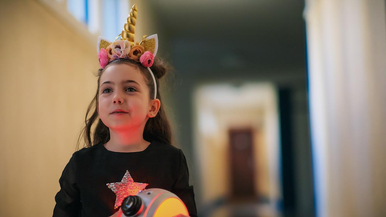 Mia mit Einhorn-Haarreif hält ein rundes, rot leuchtendes Gerät in einem Flur.