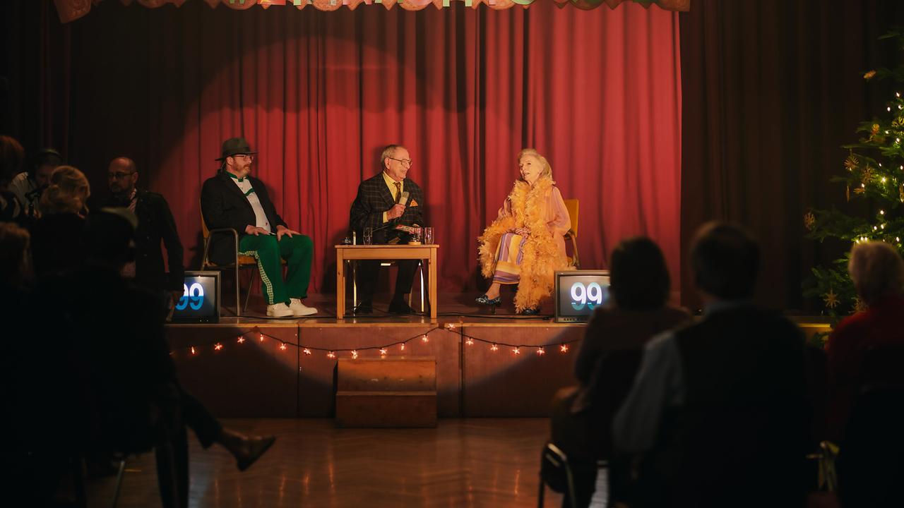 Kurt Bäuchlein, Paul Papp und Mathilde Eisenhut sitzen auf einer kleinen Bühne vor Publikum beim Weihnachtsquiz.