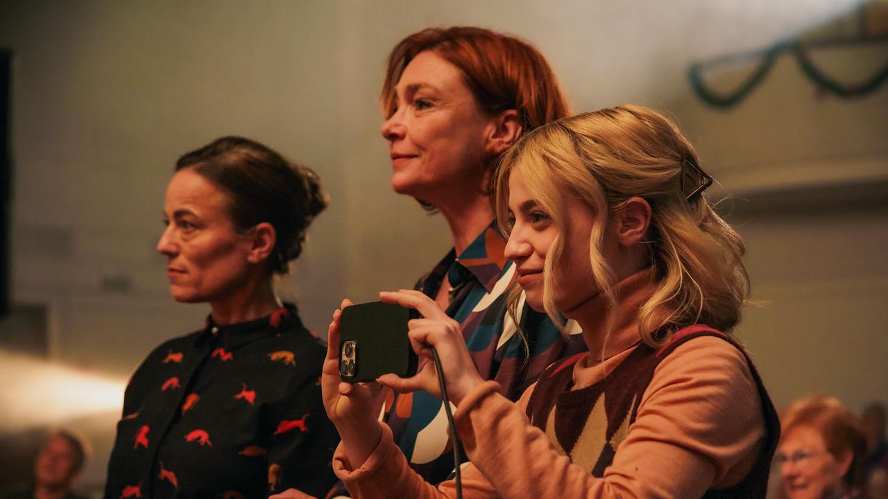 Doris Eisenhut, Gabi Eisenhut und Anna Eisenhut im Publikum stehen beim Weihnachtsquiz eng beisammen, Anna filmt die Bühnenszene mit dem Smartphone.