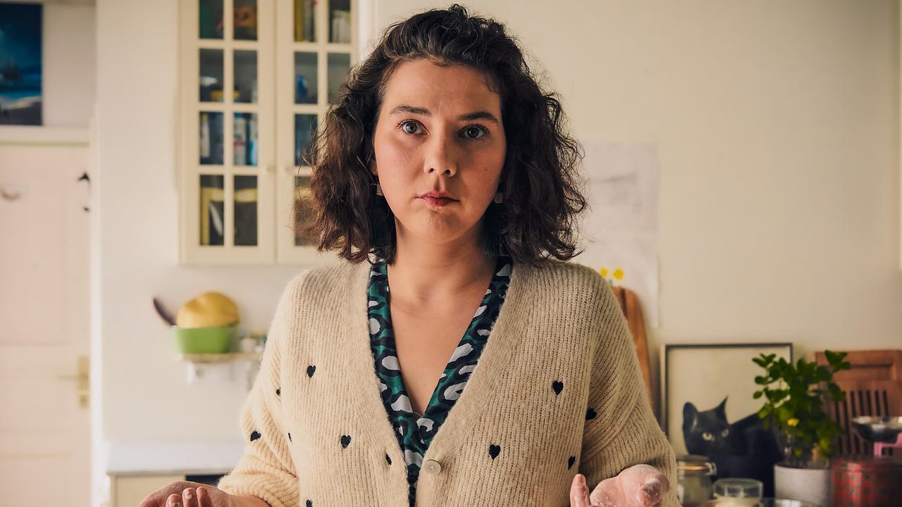 Julia steht in einer Küche mit mehligen Händen und blickt auf etwas.
