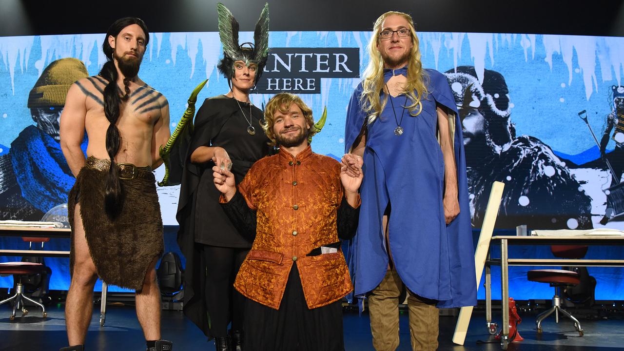 Martin Moder, Dr. Elisabeth Oberzaucher, Martin Puntigam und Dr. Florian Freistetter in fantasievollen, mittelalterlich oder mythologisch inspirierten Kostümen posieren auf einer Bühne vor winterlicher Kulisse.