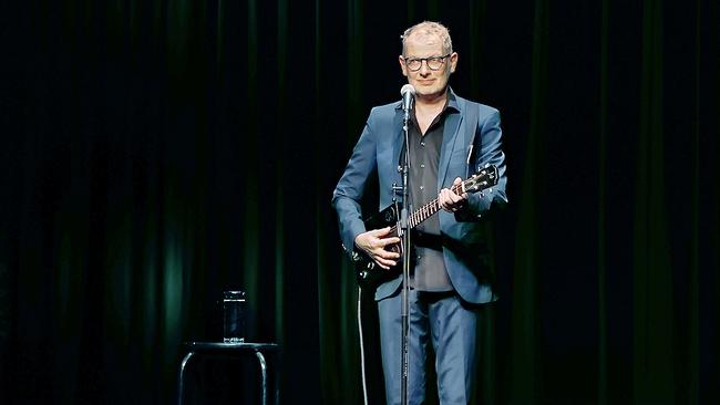 © ORF/Posthof Linz Severin Gröbner im blauen Anzug spielt auf einer dunklen Bühne Gitarre und steht dabei vor einem Mikrofon.