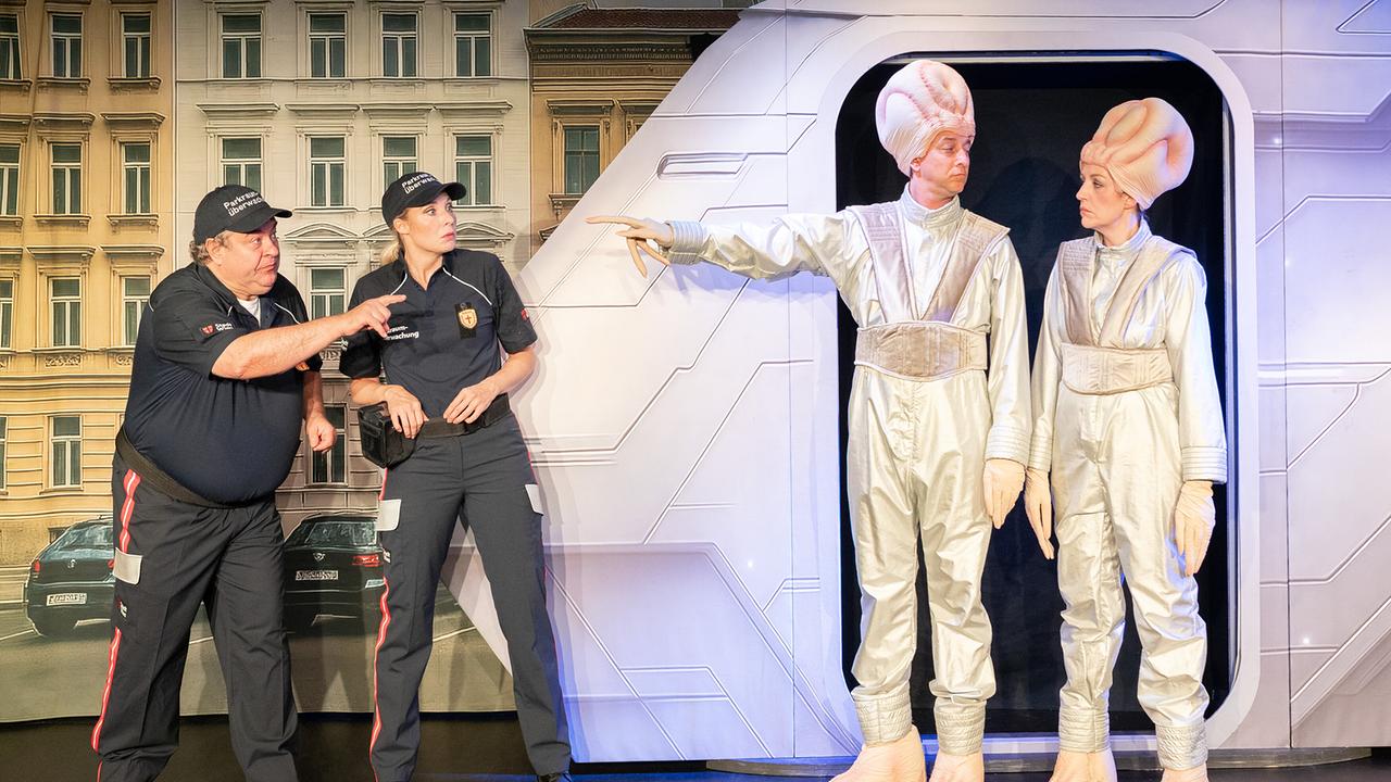 Bernhard Murg und Jenny Frankl als Parkraumüberwachende treffen vor einem futuristischen Raumschiff auf zwei seltsam kostümierte Außerirdische dargestellt von Julian Loidl und Katharina Dorian.