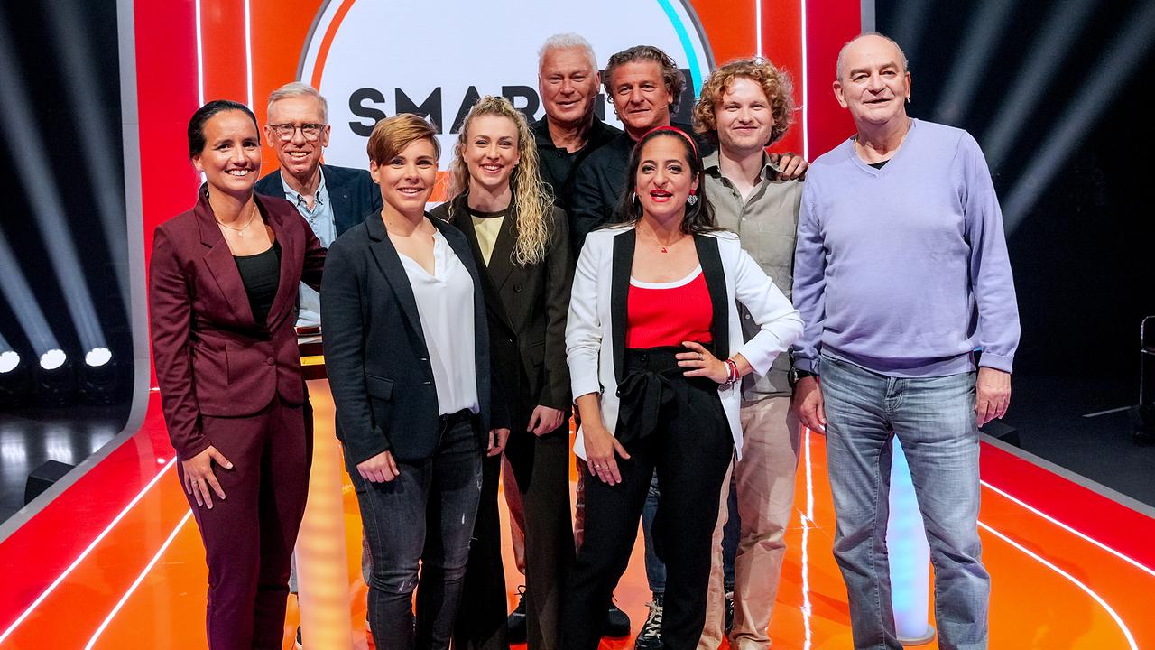 © ORF/Roman Zach-Kiesling Gruppenfoto mit Irene Fuhrmann, Nici Schmidhofer, Peter Stöger, Alina Eberstaller, Toni Polster, Peter Moizi, Caroline Athanasiadis, Dr. Bohl und Herbert Prohaska auf einer hell ausgeleuchteten "Smart10 BIG"‑Studio‑Bühne mit auffälligem orange‑rotem Design.