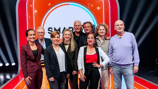 Gruppenfoto mit Irene Fuhrmann, Nici Schmidhofer, Peter Stöger, Alina Eberstaller, Toni Polster, Peter Moizi, Caroline Athanasiadis, Dr. Bohl und Herbert Prohaska auf einer hell ausgeleuchteten "Smart10 BIG"‑Studio‑Bühne mit auffälligem orange‑rotem Design.  