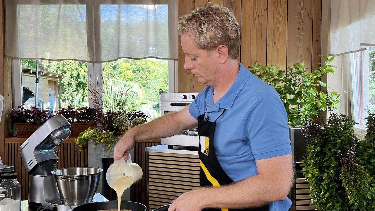 © ORF/On Media Fritz Treiber steht in einer Küche und gießt Waffel-Teig in eine Pfanne