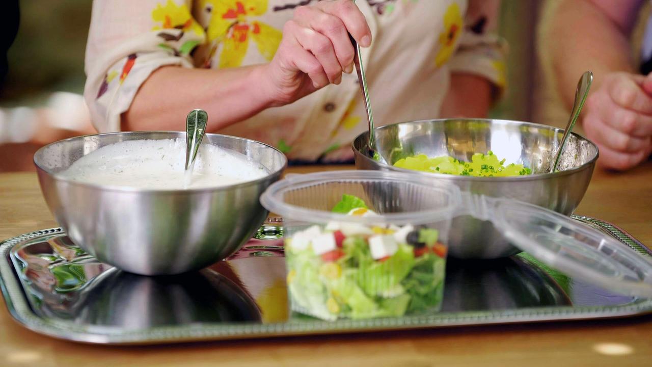 Schüsseln mit Salaten und Dressing auf einem Tisch