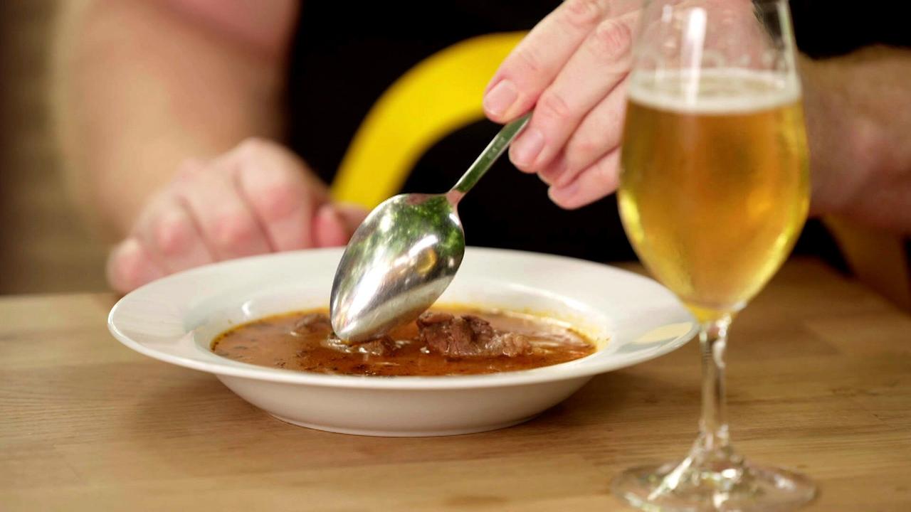 Nahaufnahme eines Tellers mit Gulasch, daneben ein Glas Bier