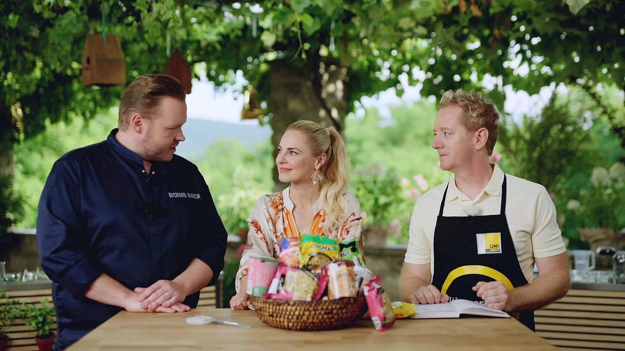 Richard Rauch, Silvia Schneider, Fritz Treiber an einem Holztisch im Freien, auf dem ein Korb mit Fertiggerichten steht