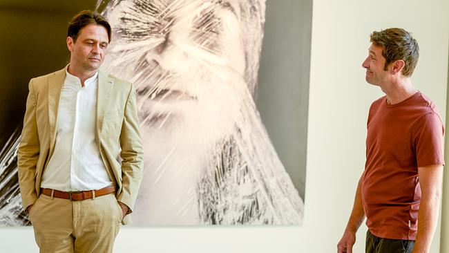 Uwe Springer und Klaus Lechner stehen in einer Kunstgalerie vor einem großformatigen Porträt einer Frau, die in Klarsichtfolie eingewickelt ist .