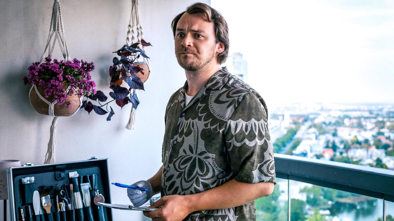 Julius Rubatsch steht auf einem Balkon, hält ein Klemmbrett und einen Kuli und arbeitet neben einem geöffneten Forensikerkoffer.