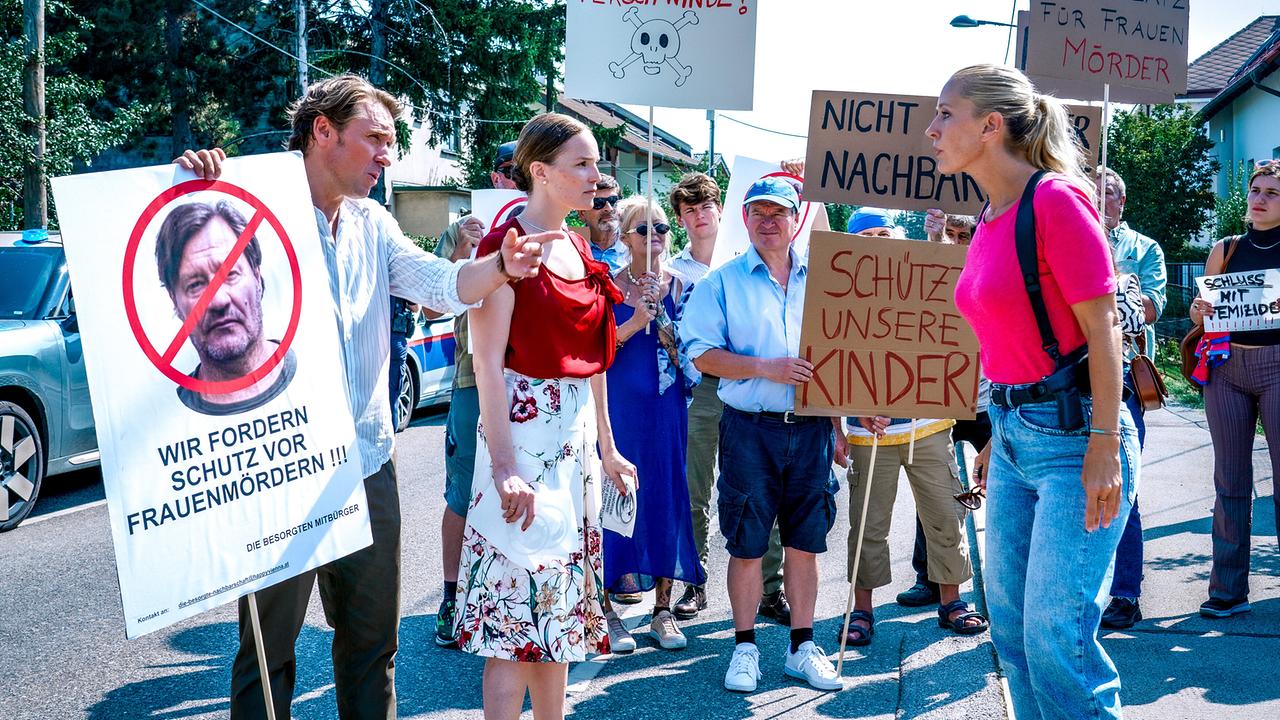 © ORF/Satel Film/Petro Domenigg Eine Gruppe von Menschen, unter ihnen Valentin Exner und Agnes Exner, demonstriert auf der Straße mit Plakaten gegen Gewalt und für den Schutz von Kindern. Penny Lanz steht vor ihnen.