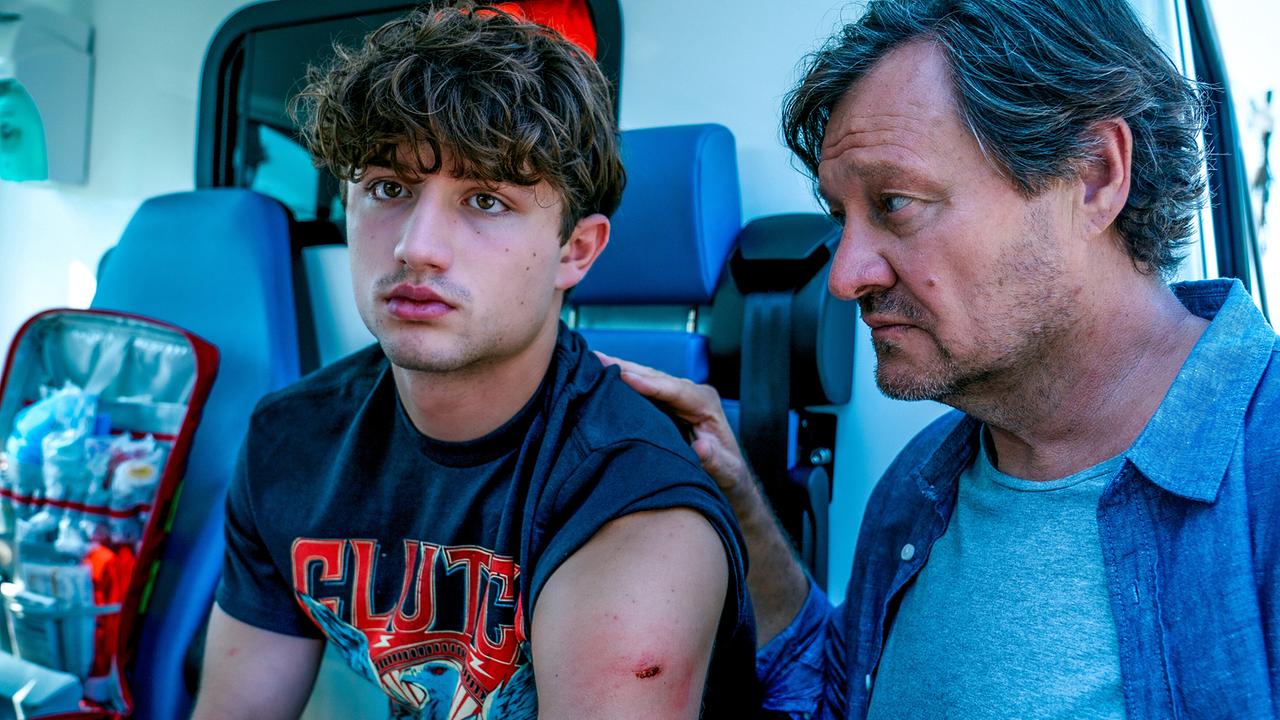 © ORF/Satel Film/Petro Domenigg In einem Rettungswagen wird der verletzte Arm des Lukas Polmer medizinisch versorgt. Gernot Polmer steht neben ihm und hat seine Hand auf dessen Schuler gelegt.