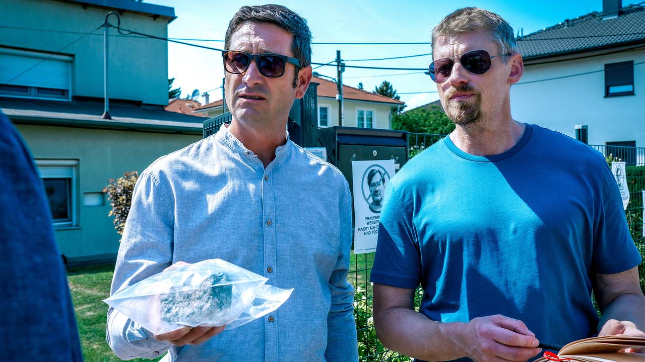 © ORF/Satel Film/Petro Domenigg Klaus Lechner und Max Herzog stehen mit Gernot Polmer im Freien auf einem Gehsteig. Lechner hält einen durchsichtigen Beutel und Gruber hält einen Notizblock.