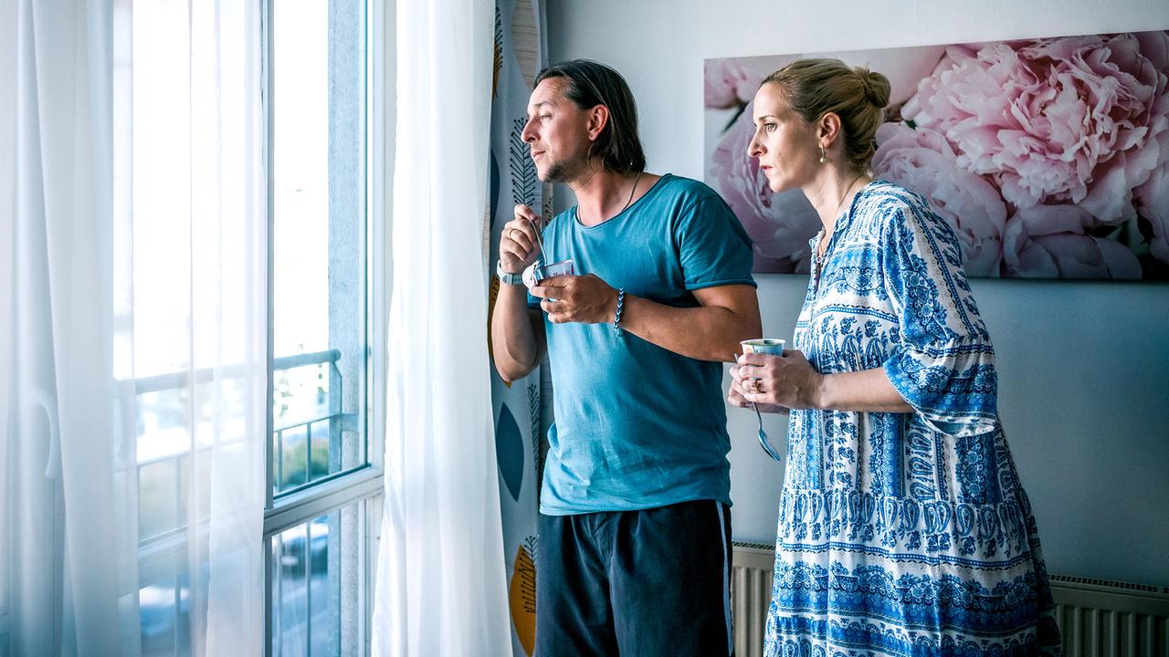 © ORF/Satel Film/Luca Breuer Christian Denk und Ines Denk stehen in einer hellen Wohnung am Fenster und schauen gemeinsam nach draußen.