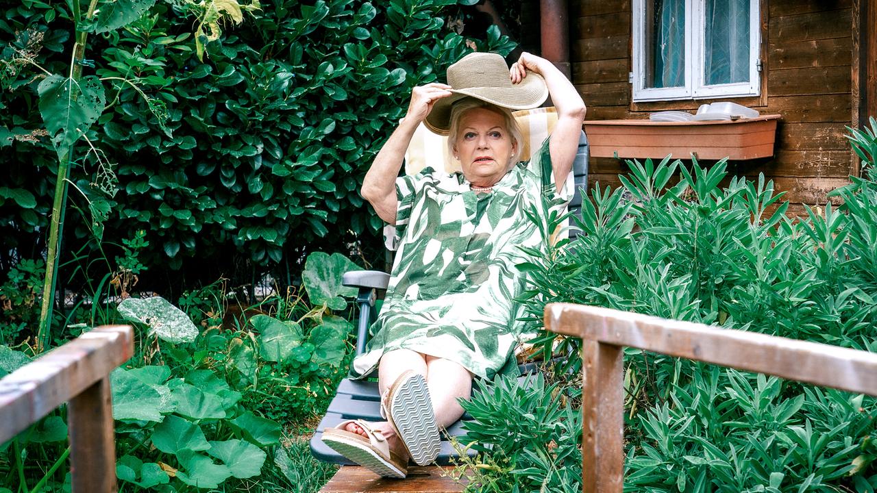 © ORF/Satel Film/Petro Domenigg Henriette Wolf liegt in einem Schrebergarten vor einer Holzhütte auf einer Gartenliege und richtet sich ihren Sonnenhut.