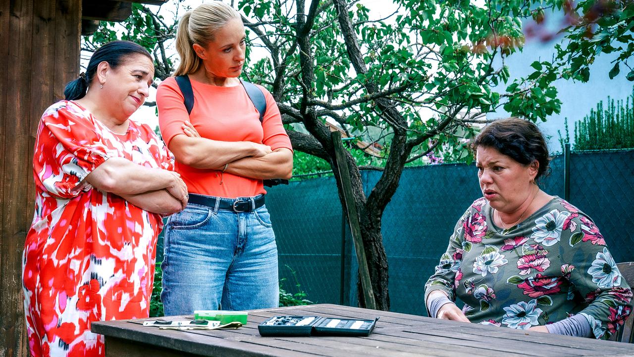 © ORF/Satel Film/Petro Domenigg Franziska Beck und Penny Lanz stehen mit verschränkten Armen an einem Gartentisch, an dem Theresa Mulsky verstört sitzt.