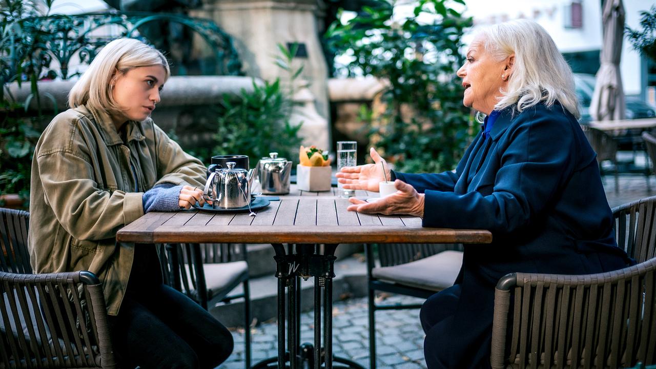 Lea Schlatterer und Henriette Wolf sitzen draußen in einem Gastgarten und unterhalten sich bei Tee.