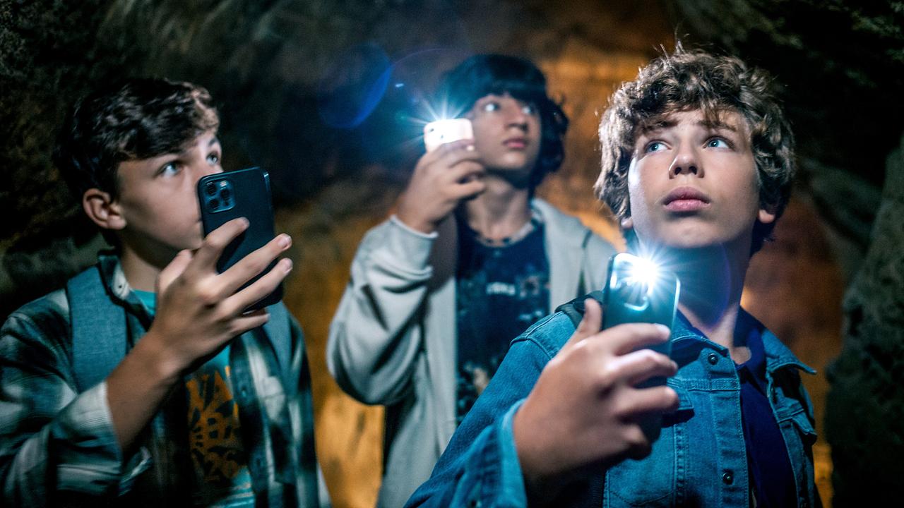 Die drei Jugendlichen Leo, Valentin und Kilian gehen mit der Taschenlampe auf ihrem Smartphones durch ein Kellergewölbe.