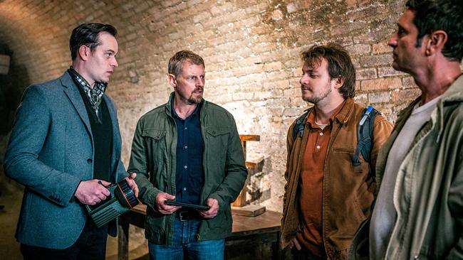 Christopfer Weigl, Max Herzog, Julius Rubatsch und Klaus Lechner stehen in einem gewölbten Kellerraum zusammen und besprechen sich.