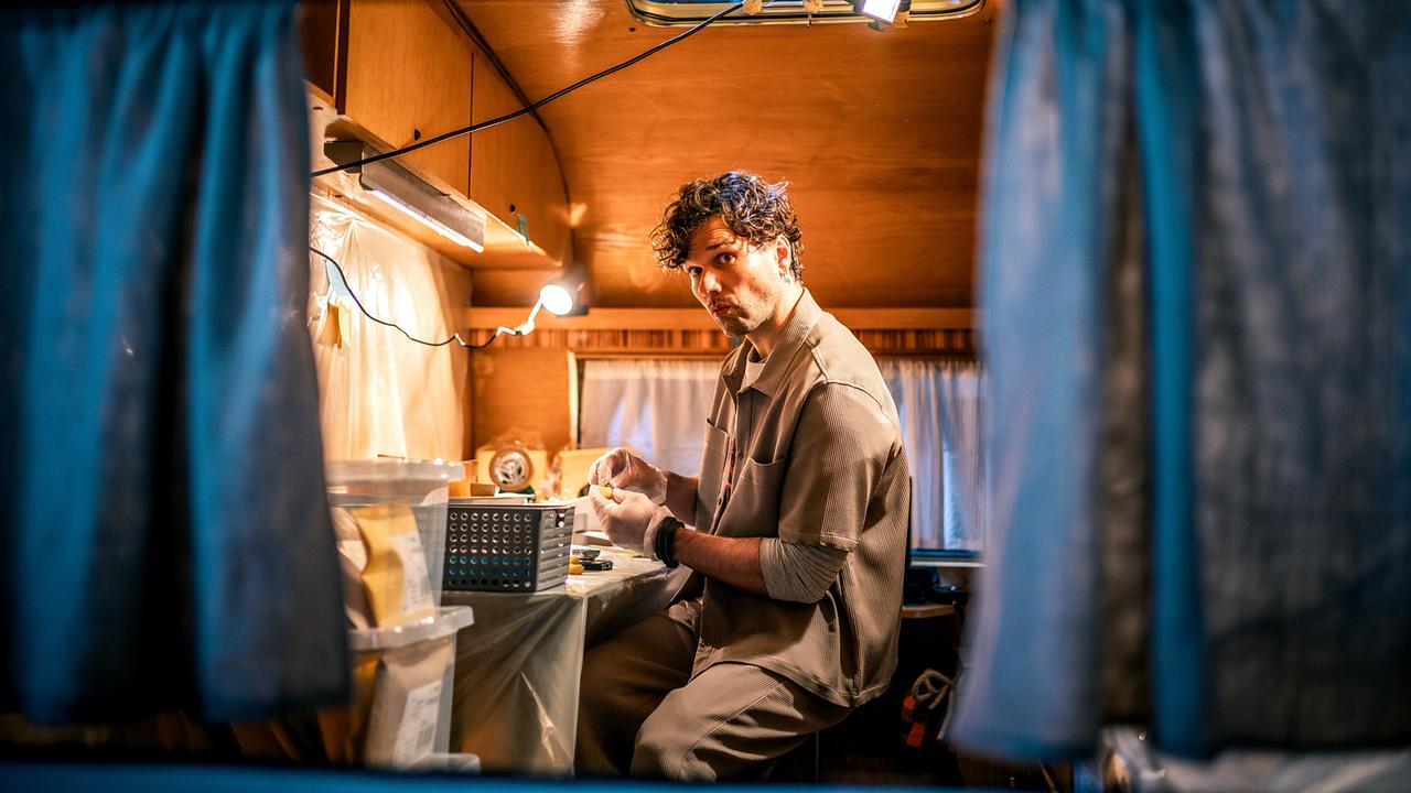 Ron Wagner sitzt in einem umgebauten Wohnwagen an einem Tisch und arbeitet bei warmem Licht mit kleinen Gegenständen.