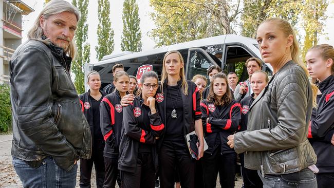 © ORF/Satel Film/Petro Domenigg Carl und Penny stehen mit einer größeren Gruppe von Spielerinnen und Erwachsenen vor einem Mannschaftsbus.