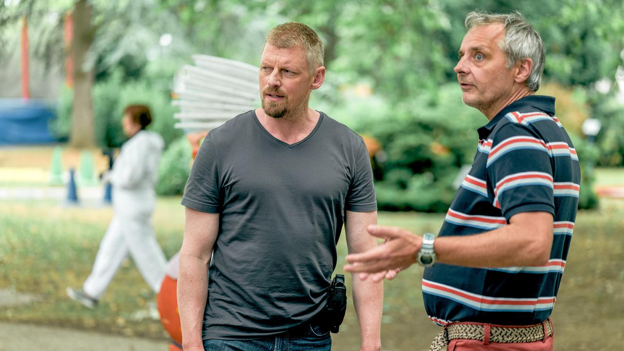 Max Herzog und René Pössl sprechen im Freien auf der Minigolfanlage vor einem abgesperrten Ermittlungsort miteinander.