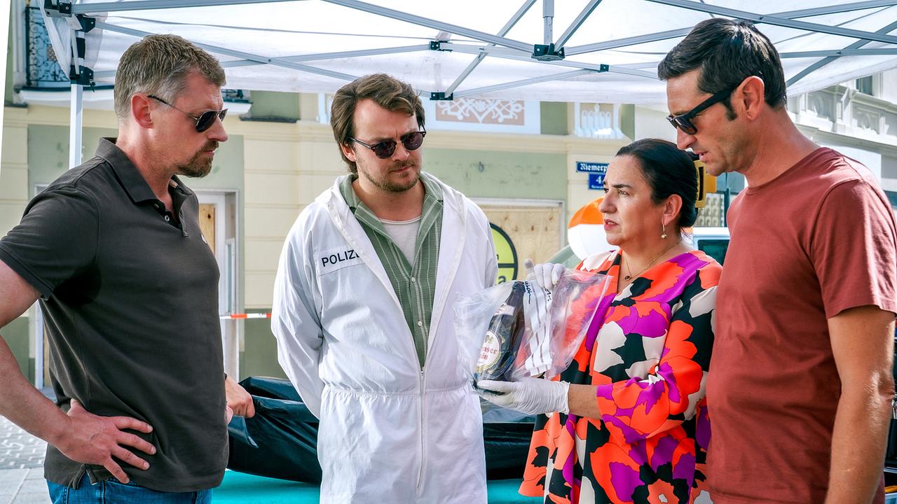 © ORF/Satel Film/Petro Domenigg Max, Julius, Franziska und Klaus stehen am Tatort unter einem Zelt und betrachten die in einem Plastikbeutel verpackte Bierflasche, die Franziska hochhält.
